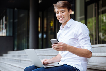 Businessman using mobile phone and laptop outdoors