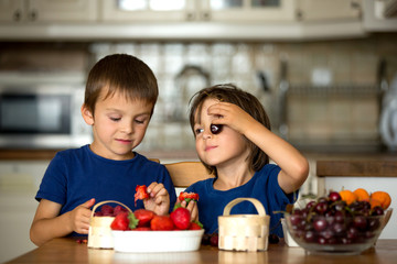 Two sweet children, boy brothers, eating fresh fruits at home