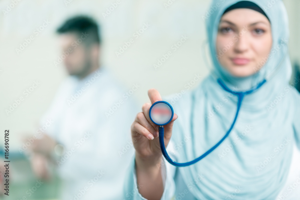 Wall mural front view of an arab doctor woman showing stethoscope.