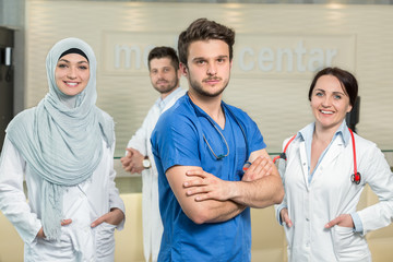 healthcare and medicine concept - attractive male doctor in front of medical group in hospital showing thumbs up