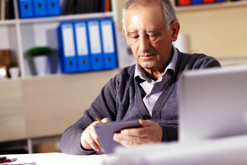 Senior businessman working in his office, he is looking something on tablet