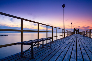 Pier on the sea at sunset. Lanterns and benches. Lonely landscape and dramatic sky.