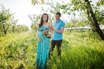 Fototapeta premium Happy pregnant couple at turquoise dress on the garden