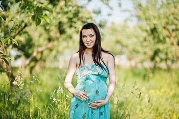 Pregnant woman on turqoise dress at green garden with high grass