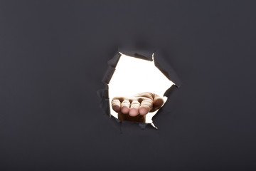 Male hand breaking through the gray paper background and holding key