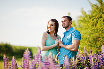 Happy pregnant couple at sunny day near violet flowers