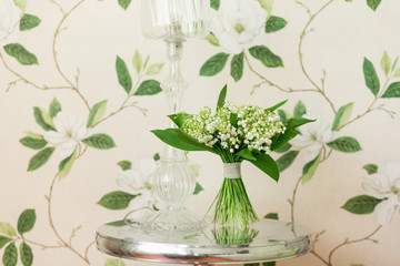 Small bouquet of Lily of the valley flowers standing on decorative metallic table. Flower decor idea. Flower design.