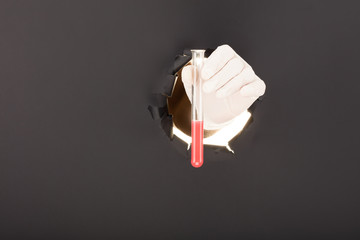 Male hand breaking through the paper background and holding test tube.
