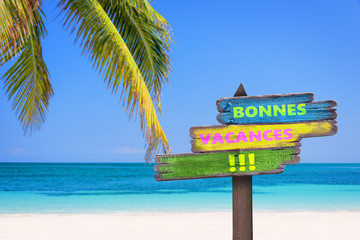 Texte Bonnes vacances écrit en français sur un panneau en bois multicolore, fond plage tropicale...