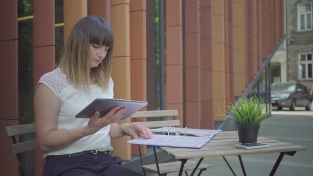 Businesswoman taking notes form folder to tablet, outdoor. Steadicam shot.
