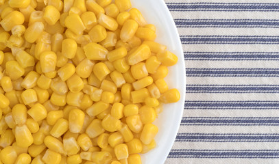 Organic sweet corn on a white plate atop a striped tablecloth.