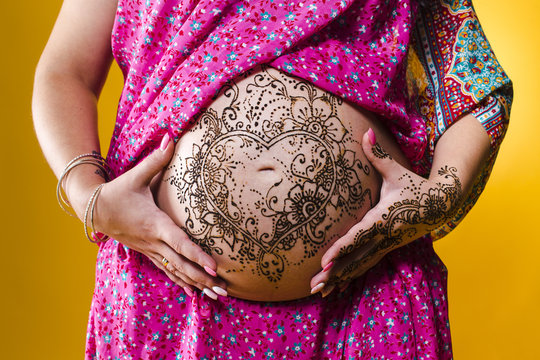 A color photo of a henna tatoo on a woman's pregnant belly, on yellow background.
