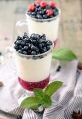 Fototapeta na wymiar Delicious parfait dessert with bilberry, milk souffle and jello layers. Frozen treat in a glass on rustic wooden background