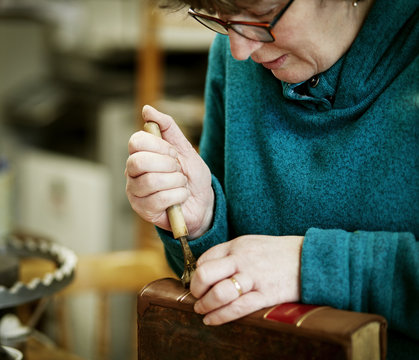 A woman working on the spine of a bound book with a hand tool.