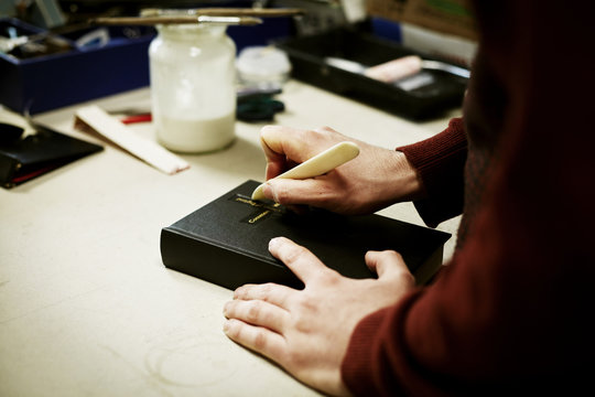 A man using a small handheld tool on the cover of a book. 