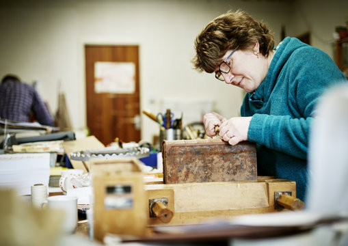 A woman working at a bench on the binding of a book in need of restoration. 
