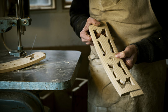 Man working in furniture maker's workshop holding shaped carved chair back struts