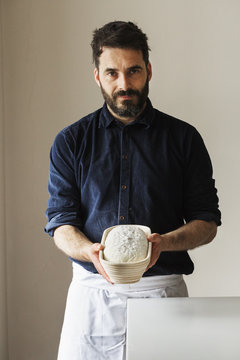Baker holding a freshly baked loaf of white bread in a rattan proofing basket.
