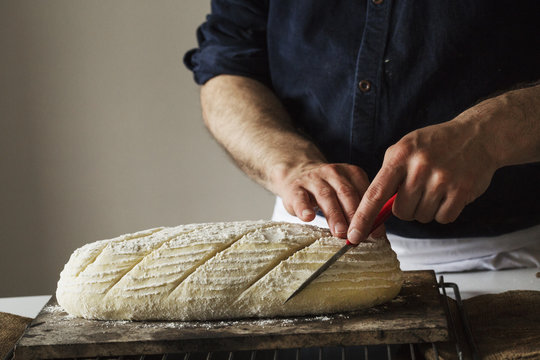 Close up of baker slicing freshly baked loaf of bread with bread knife
