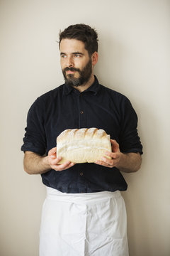 Baker holding a loaf of freshly baked white bread.