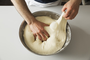 Close up of a baker kneading bread dough in a metal bowl.