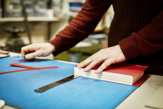 A man working on a bench, to measure and cut the material for recovering a book, in a bookbinding workshop. 