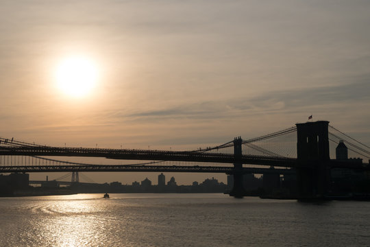 Dark silhouettes of sections of Brooklyn, Manhattan and Willamsburg bridge at dawn with sun low in the sky