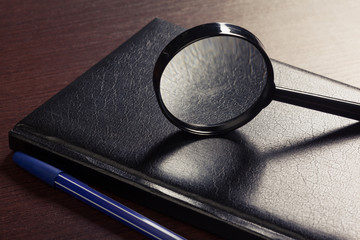 Magnifying glass and book o the wooden background