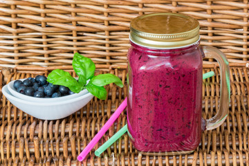 Healthy Breakfast. Blueberry smoothie in a mason jar and fresh juicy blueberries on a wicker table. Selective focus
