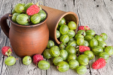 Freshly picked raspberries and gooseberries.   Freshly picked raspberries and gooseberries in a clay mug and in a glass on a wooden table.