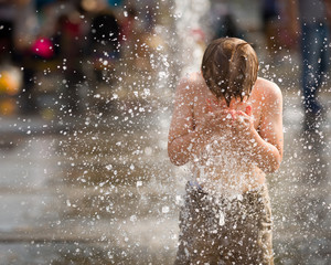 Fototapeta premium Portrait of cute kid boy playing with fountain on the street on a sunny day. Child having fun outdoors.