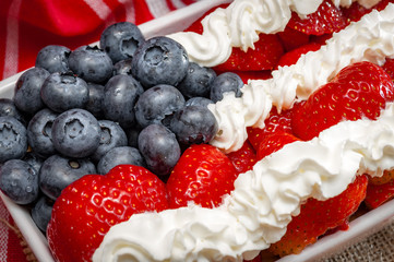 Whip Cream, strawberries and blueberries combined to look like the american flag and placed in a ceramic tray  for a 4th of july themed party, on a wooden table and rustic towel