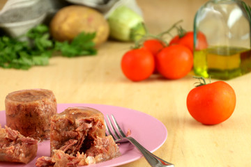 A pink dish with famous italian leancheon meat. Background: tomatoes, potato, zucchini, parsley, a bottle of olive oli and a linen cloth.