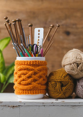 Jar with knitted cover holding different sized knitting needles and crochet hooks.