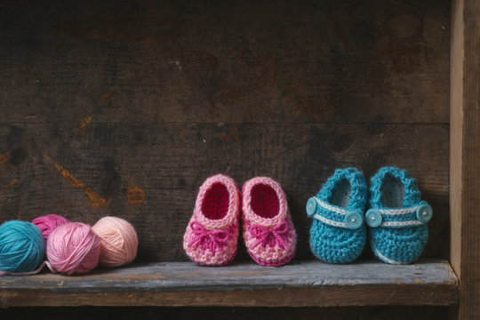 Crochet baby booties with knitting yarn on a wooden shelf.
