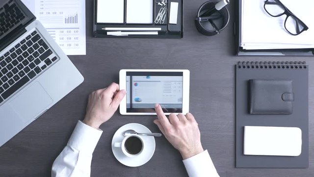 Businessman working at office desk and using a touch screen tablet, he is checking financial reports and using mobile apps