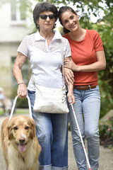 Senior blind woman walking with help of dog and carer