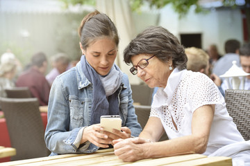 Senior woman and home carer at cafŽ terrace using smartphone