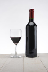 Botella de vino y copa sobre mesa de madera blanca