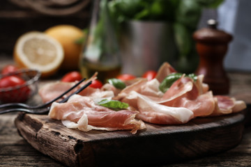 thin slices of prosciutto with mixed with basil, cherry tomatoes on wooden cutting board,vintage background