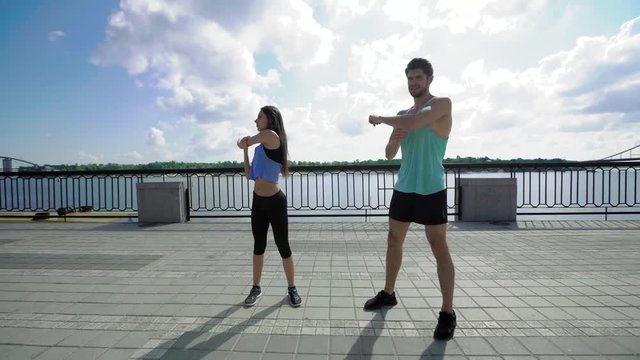 Attractive people working out on the bridge, warm-up and stretching of the arms and shoulders