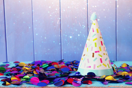 Party hat and colorful confetti on wooden table
