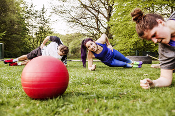 People doing side plank on grassy field at park