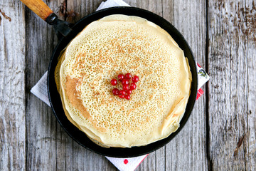Russian traditional pancakes in a cast iron frying pan on a wooden background