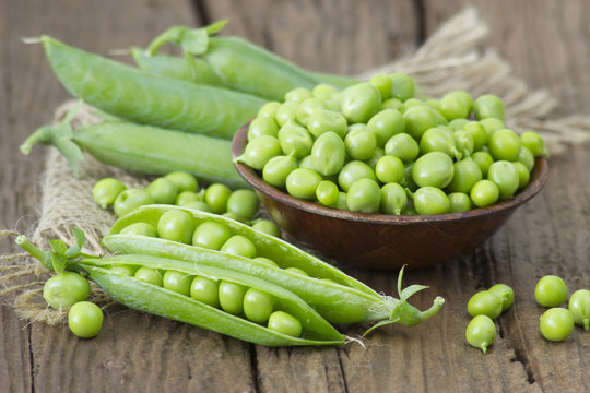 a bowl full of green peas on wooden background