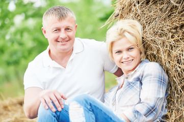 smiling adult couple near haystack at countryside