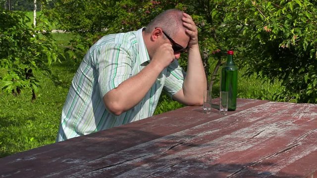 Man crying near bottle of alcohol on table