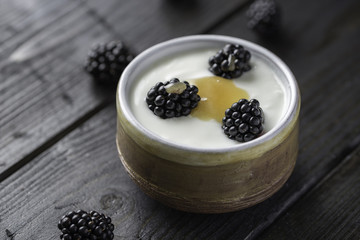 Fototapeta na wymiar Closeup of blackberries with honey, white yogurt in brown bowl on black wooden table.