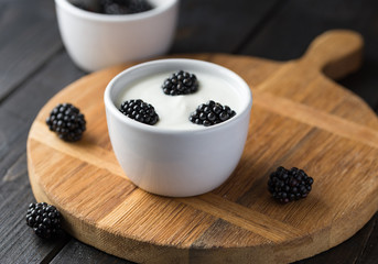 Blackberries in white yogurt on natural cutting boards and wooden black table.