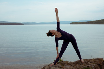 Young woman is practicing yoga at mountain lake